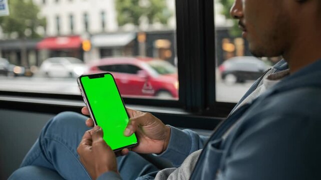Person using smartphone with green screen sitting by window in urban environment during daytime