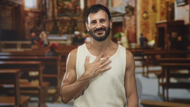 Man with hand on chest touching and smiling in ornate church building, wearing sleeveless tanktop; gratitude reflection.