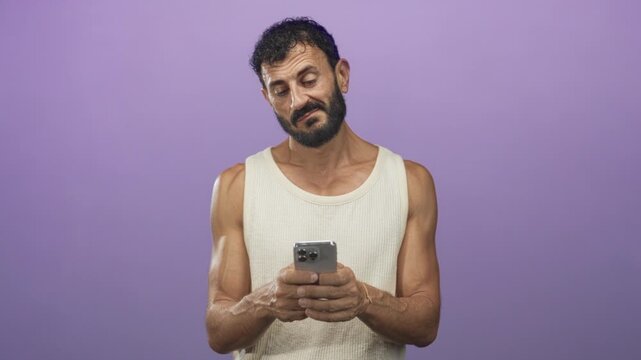 Man texting on smartphone with both hands, forearms exposed and a slight smirk in a studio setting wearing a sleeveless tanktop; bemusement casual.
