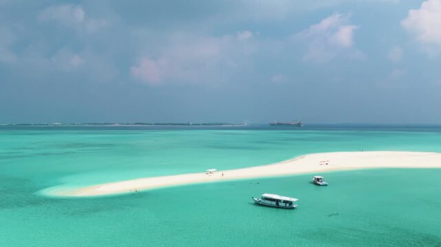 Aerial view of a pristine white sandbank surrounded by crystal clear turquoise water with two boats anchored nearby in Vashafaru, Haa Alif, Maldives.