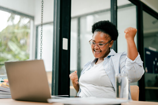 Black woman celebrating online success with laptop