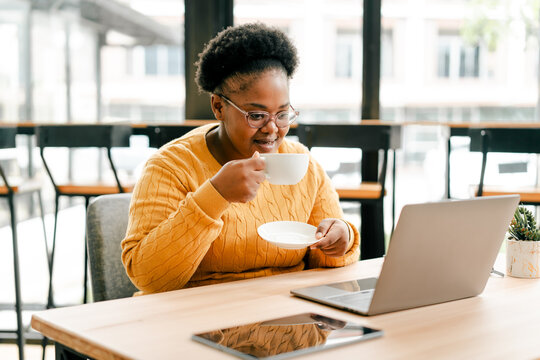 Black woman relaxing with coffee watching laptop
