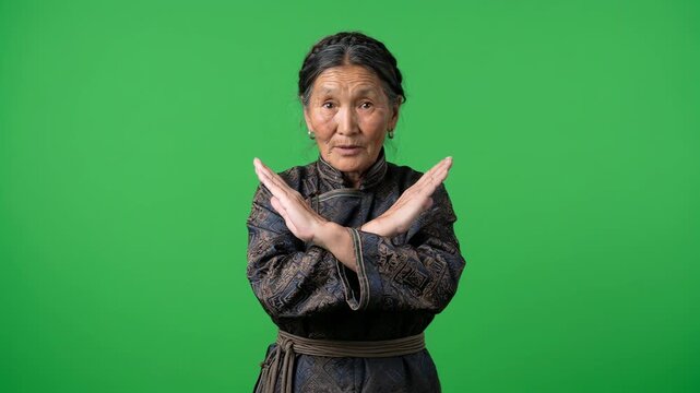 Elderly Mongolian Woman Making X Shape Gesture with Arms on Green Screen for Rejection or Stop Concept