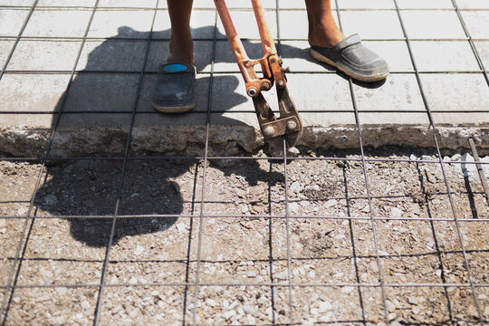 Construction worker uses heavy duty orange bolt cutters to trim steel rebar mesh.