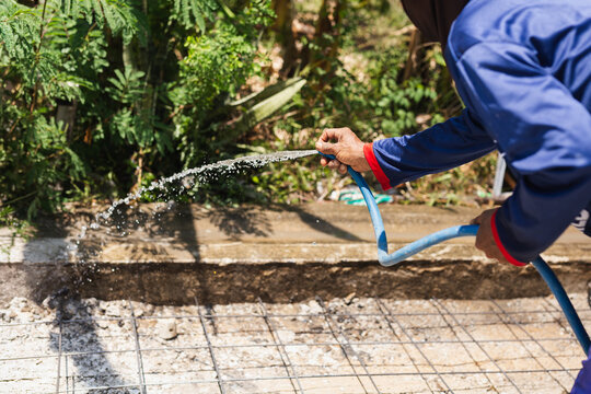 Construction worker spray water over steel reinforcement mesh preparing the ground for concrete pouring.