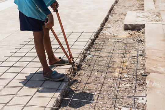 Construction worker uses heavy duty orange bolt cutters to trim steel rebar mesh.
