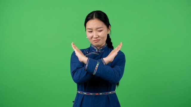 Young Asian Woman in Traditional Blue Dress Making X Sign with Arms Expressing Refusal Rejection or Disagreement Standing over Green Screen Background for Commercial and Educational Use