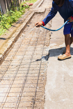 Construction worker spray water over steel reinforcement mesh preparing the ground for concrete pouring.