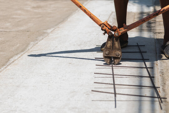 Construction worker uses heavy duty orange bolt cutters to trim steel rebar mesh.