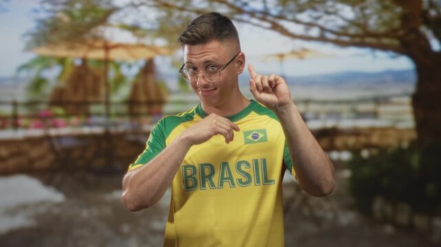 Man wearing brasil soccer shirt points finger and taps chest in studio with staged tropical backdrop and props; pride celebration fan support.