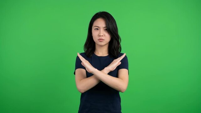Asian woman making X sign with crossed arms and turning head away in rejection or denial gesture for advertising and social media content on green screen background