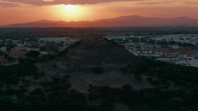 Aerial backward dolly overlooking El Cerrito ancient pyramid in Santiago de Queretaro, Mexic at sunset