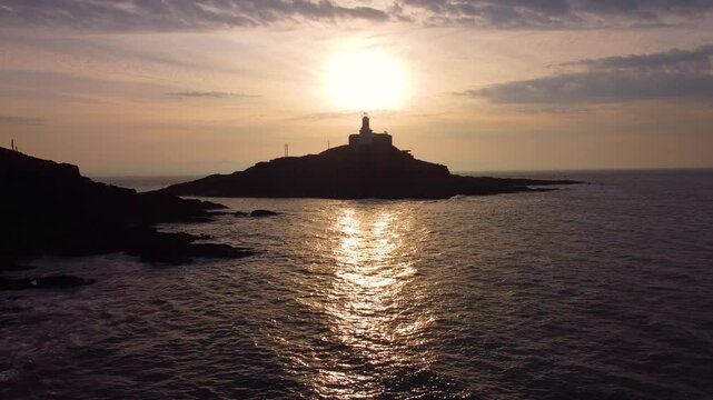 Silhouette of Mumbles Lighthouse at Sunrise. Golden Reflection of Sun on Ocean with Dynamic Clouds. Perfect for tourism, travel documentaries. Wales, UK. 4K.