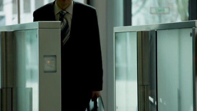 Businessperson in suit with briefcase walks through glass security turnstile in lobby