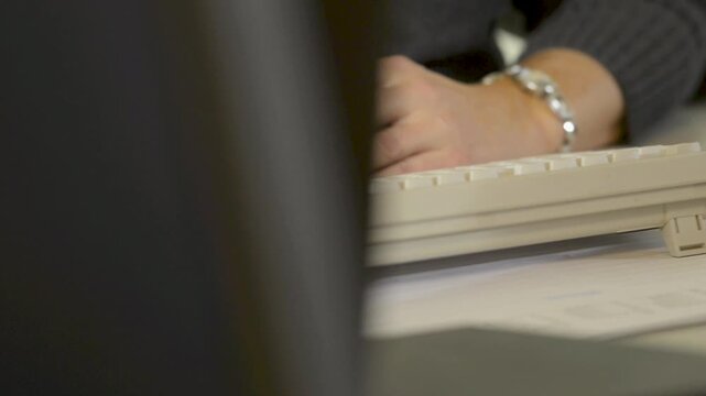 Hands typing on computer keyboard at desk with papers, close up office scene