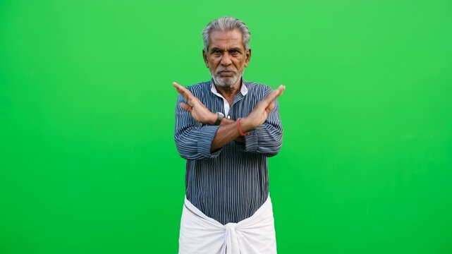 Senior Indian man making stop or no sign with crossed arms as X symbol for rejection and denial on green screen background for chroma key compositing