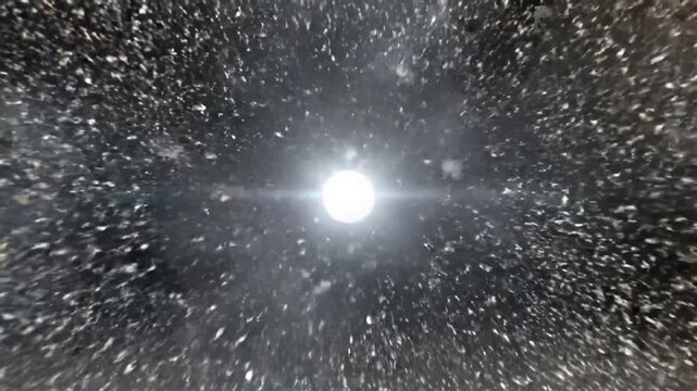 A bright white star-like object radiating light in the center of a dark, speckled cosmic background, resembling a distant galaxy or nebula.
