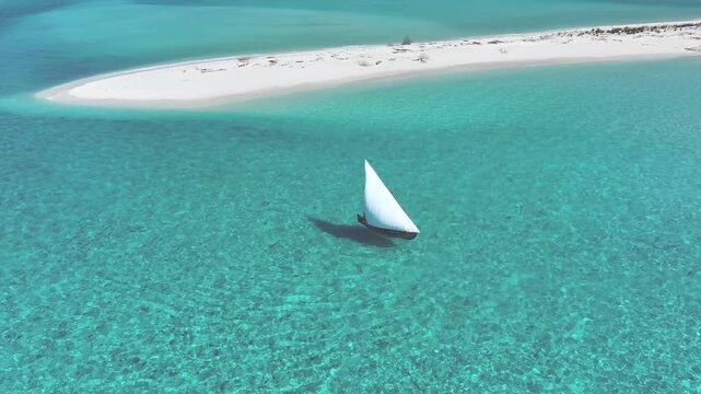 Aerial view of a traditional boat sailing through turquoise waters near a white sandbank in Bileffahi, Shaviyani Atoll, Maldives.