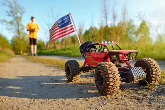 Remote control off-road car with American flag on a dirt path, child playing outdoors, summer hobby, adventure and leisure concept