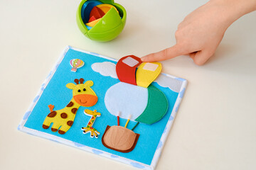 Obraz premium Child playing with colorful felt activity board featuring giraffe and hot air balloon, fine motor skills educational toy on white background