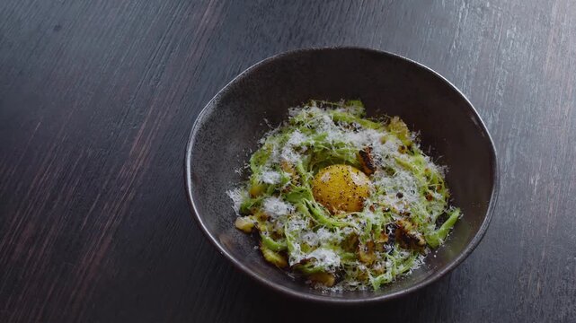 Gourmet pasta dish with egg yolk and grated cheese served in a dark bowl