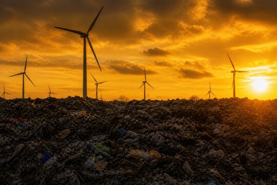 A silhouette of modern wind turbines at sunset, standing on an old landfill full of plastic waste, a theme of wildlife conservation. Environmental protection
