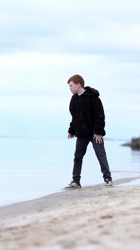 A teenager enjoys a fascinating game of throwing stones into the water of a lake, sea, or ocean. The boy relaxes, playing with stones and pebbles, throwing them into the lake. 