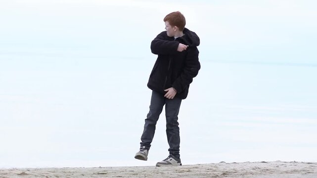 A teenager enjoys a fascinating game of throwing stones into the water of a lake, sea, or ocean. The boy relaxes, playing with stones and pebbles, throwing them into the lake. 