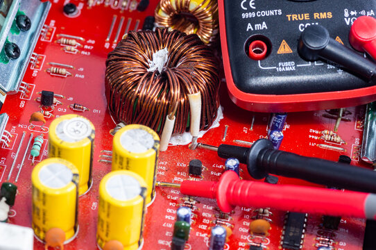 A multimeter with test probes and a circuit board lie on a white background.