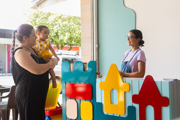 Two adult women and a baby entering a colorful early childhood stimulation center, reflecting care,...