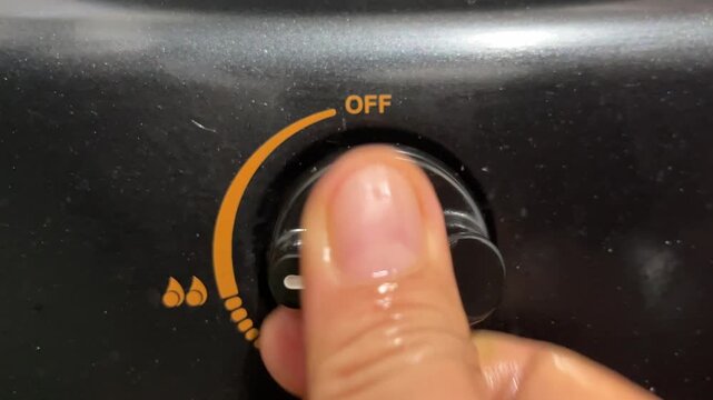 Close up of a hand turning the knob of a gas stove to the on position
