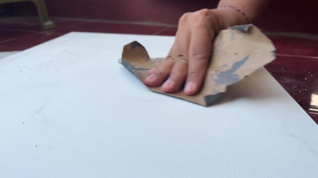 Close up of an artist's hand sanding a white primed canvas with sandpaper