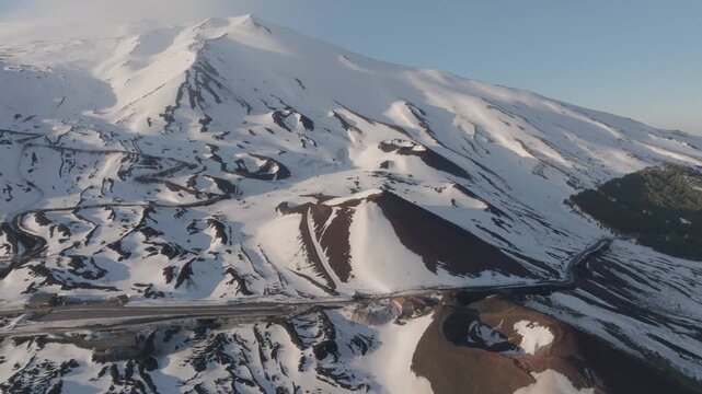Aerial view of Rifugio Sapienza and the snow-covered volcanic landscape with winding roads and craters on Mount Etna in Nicolosi, Sicilia, Italy.