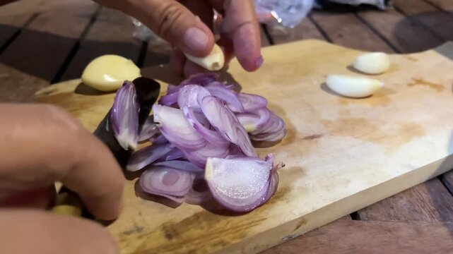 Close up of hands preparing and slicing red shallots on a wooden cutting board