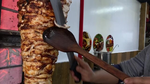 Chef Slicing Roasted Chicken Shawarma Meat from Vertical Grill Rotisserie