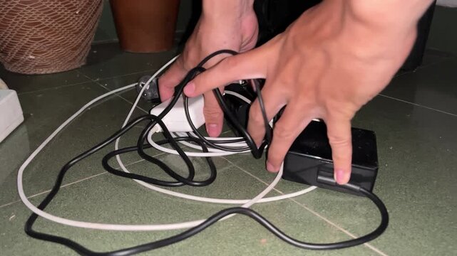 Close up of hands trying to organize a messy pile of tangled electronic cables and power adapters