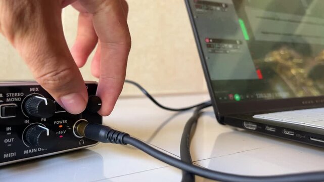Close up of a hand adjusting the volume knob on an external USB audio interface soundcard
