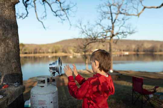 boy warming hands by a portable propane heater at a lakeside campsite