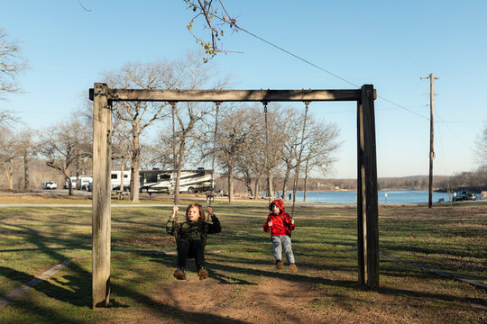 Two children playing on a wooden swing set at a campground near a lake
