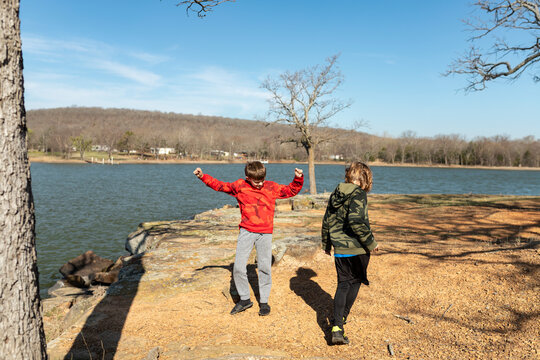 Two boys playing on a rocky shoreline of a lake during the day
