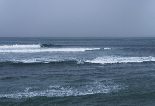 Lone surfer riding wave on overcast day, Uluwatu, Bali