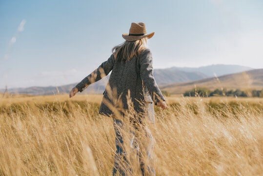 Blond woman in hat and blazer in golden field at sunset with mountains