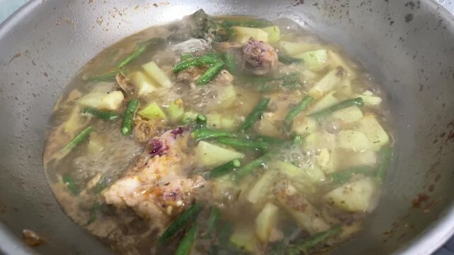 Close-up of hot vegetable and meat soup boiling with rising steam inside a stainless steel cooking pan.