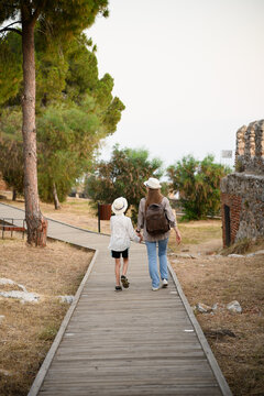 Mother and son walking together on a wooden path in a park. Family travel and tourism concept, woman with child exploring ancient ruins, summer vacation and outdoor leisure, rear view