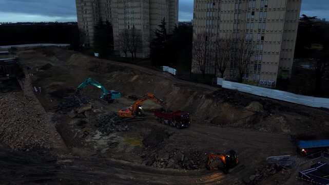 Aerial view of heavy machinery, including excavators and truck, working on demolition site at evening