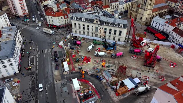 High angle drone view of busy construction site with cranes, cement mixers, and workers in city center of Paris, France