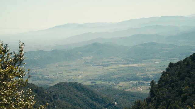 A wide view from the Spanish countryside reveals layered mountain ridges, patchwork farmland, and soft atmospheric haze stretching across a vast rural landscape.