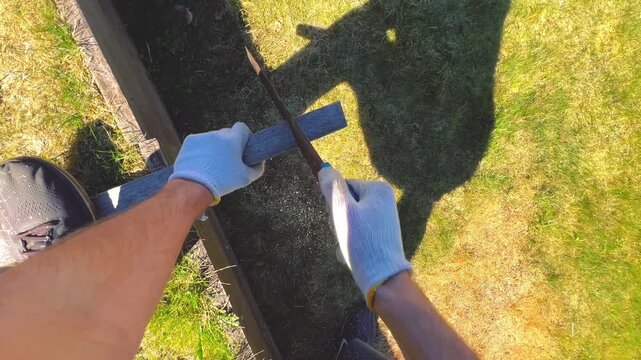 First-person perspective of worker in gloves cutting timber on a lawn. Ideal for DIY home improvement tutorials, hardware store advertisements, and construction safety videos.