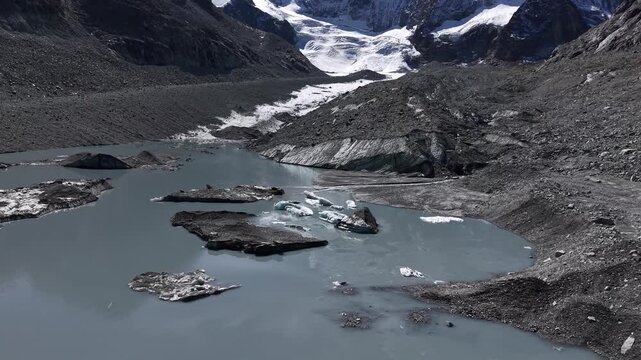 Aerial flyover over the glacial lake of Glacier de Cheilon with a pan up view from the icebergs and moraines to the mountain peaks of the Swiss Alps