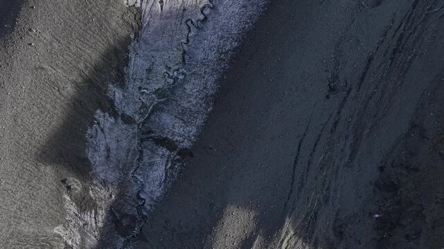 Aerial flyover over ice of Glacier de Cheilon on a sunny summer day in the Swiss Alps with a pan up view towards the mountain peaks of Arolla such as Mont Blanc de Cheilon